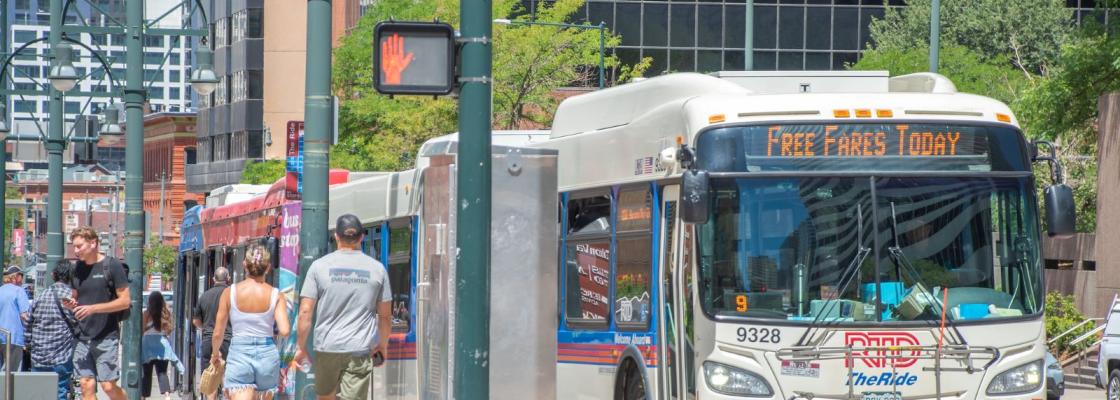 A Regional Transportation Bus stopped at a red light with people walking on the sidewalk adjacent to it.