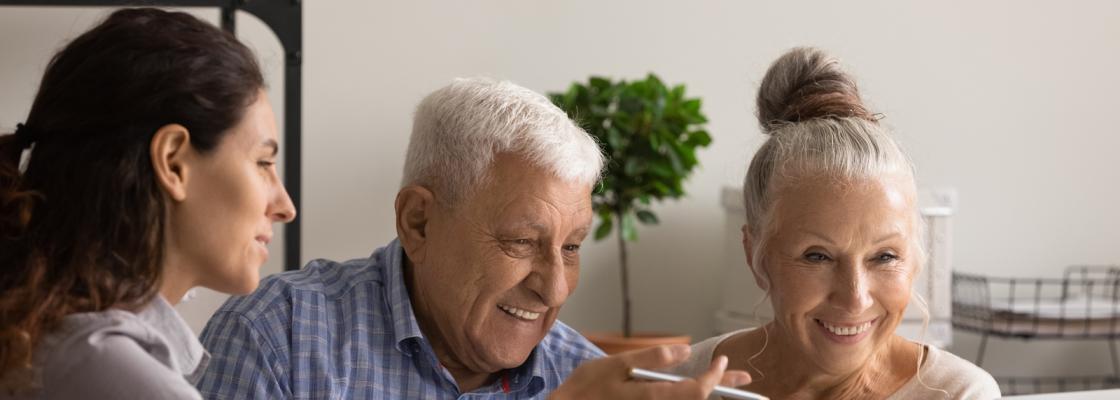 A husband and wife, who are older adults, sit at a table with a younger woman, who is a case worker, to discuss resources available for aging adult.