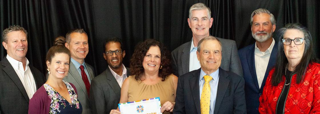 A group of smiling people stands in front of a black backdrop. One is holding a certificate that says Metro Vision Award.