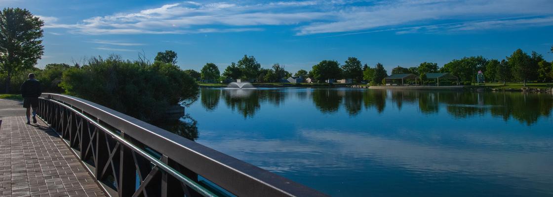 A pedestrian crossing a small bridge over a lake.