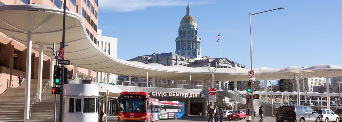 Buses at a bus station with the Colorado State Capitol dome in the background.
