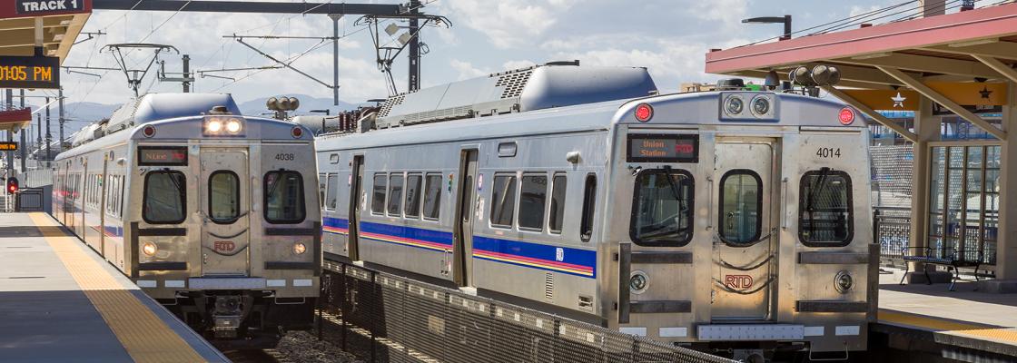 Two commuter rail trains at a station on two tracks separated by a fence.