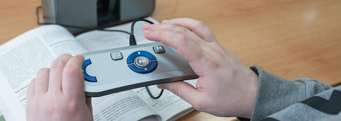 Hands holding a scanning and reading machine that is being used to read a book.