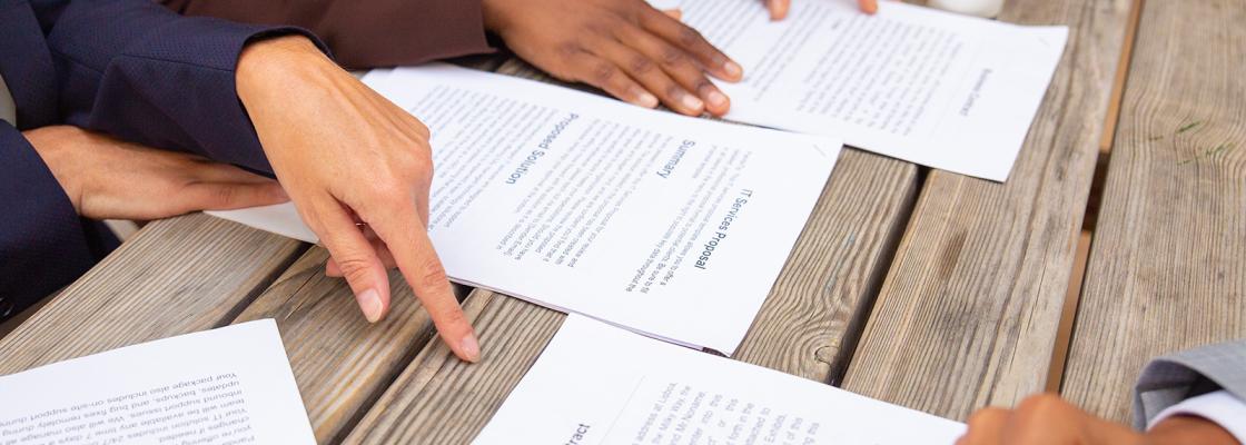 Close-up view of hands holding and pointing to pieces of paper sitting on a wooden table.