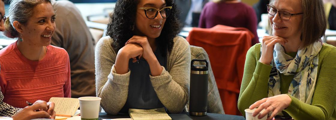 Three people are sitting around a table in a crowded conference room discussing growth and development topics affecting the Denver region.
