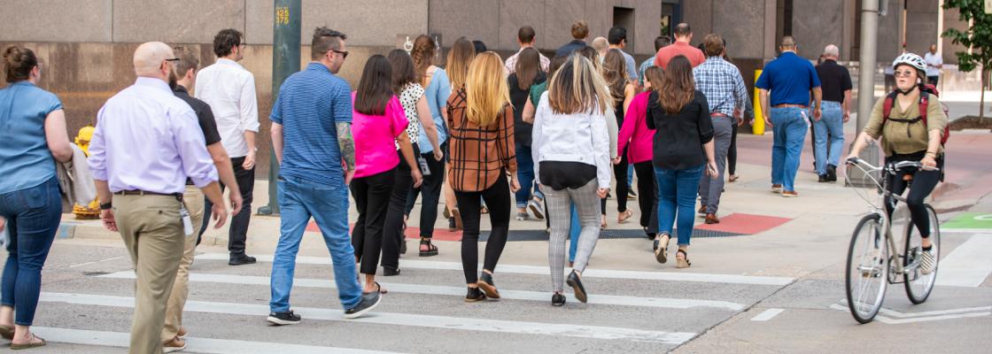 A group of people crossing a crosswalk on a city street next to a cyclist riding a bike in a bike lane.