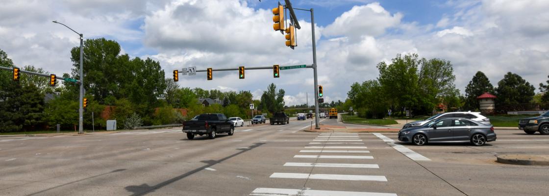 Cars and trucks driving through and waiting at a stoplight at a large intersection.