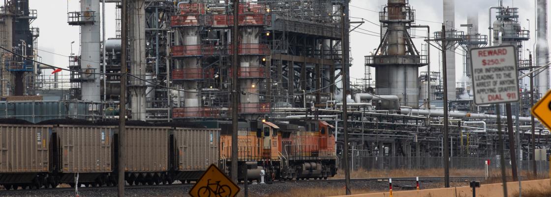 A freight train traveling down tracks next to a power plant.