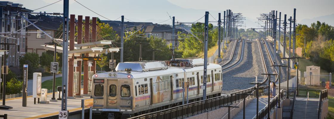 A commuter rail train pulling into a suburban station with hazy mountains in the background. Photo credit: Photo courtesy of RTD.