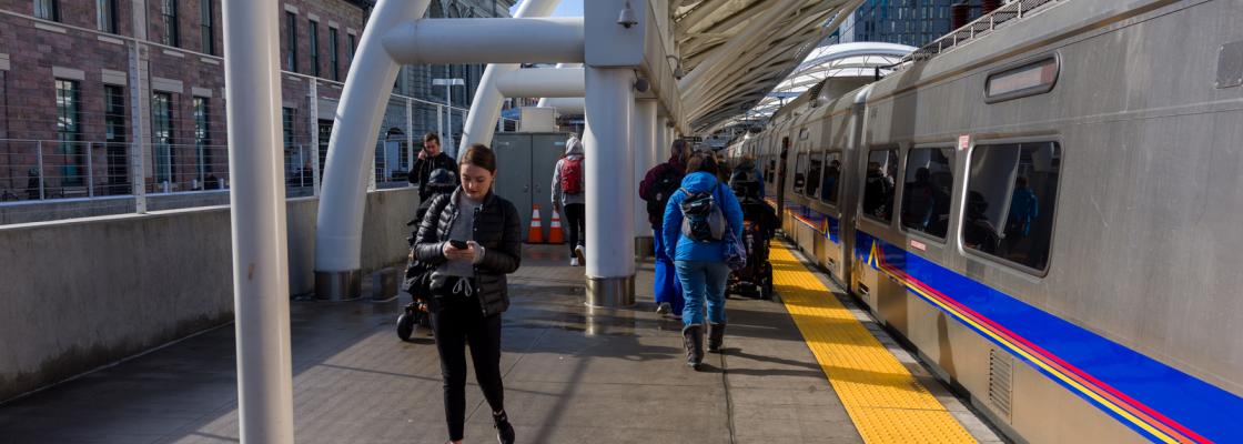 People walking on a train platform next to a commuter rail train at Union Station in Denver.