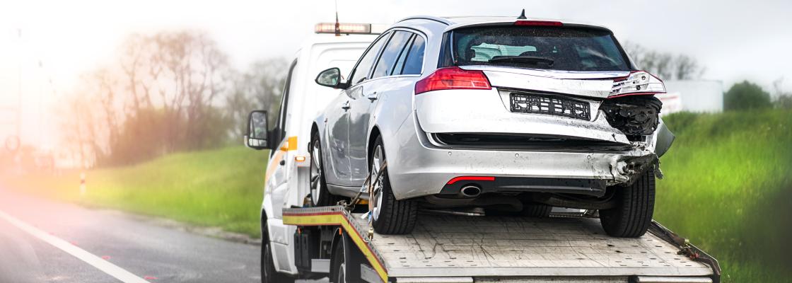A flat-bed tow truck transposrts a SUV that has rear damage on its rear. 