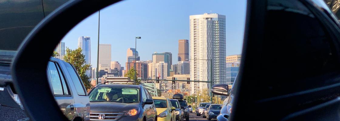 The downtown Denver skyline seen from the side-mirror of a vehicle. 