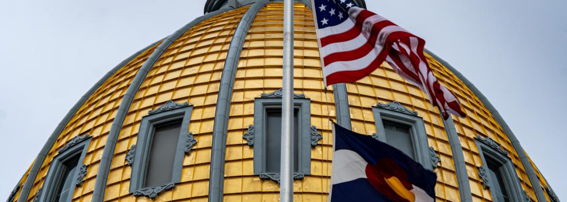 A close-up of Colorado's gold-domed capitol, with the American and Colorado flags in the foreground.