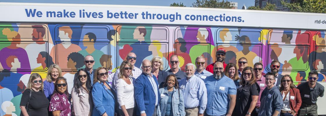 A diverse group of people stand in front of a bus. 