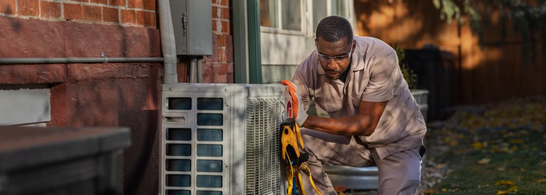 HVAC technician installing a heat pump in a backyard next to a brick wall